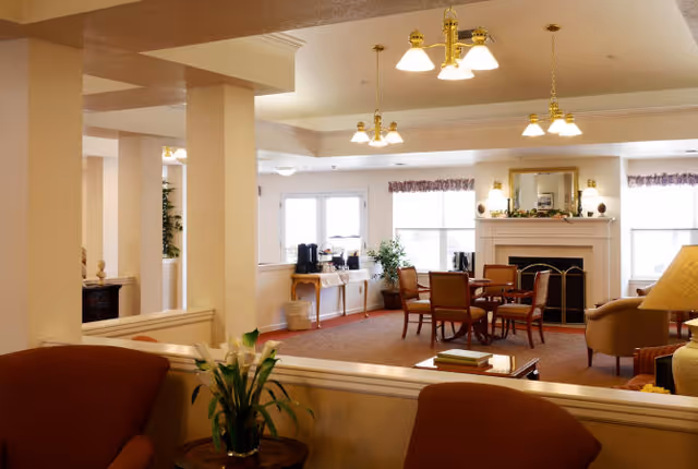 Bright communal lounge with seating, tables, a fireplace, and a coffee station near windows.