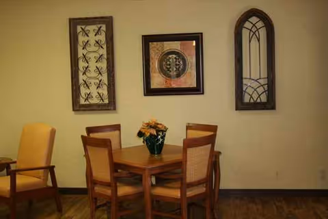Wood dining table with four chairs and wall art in a cozy senior living dining area.