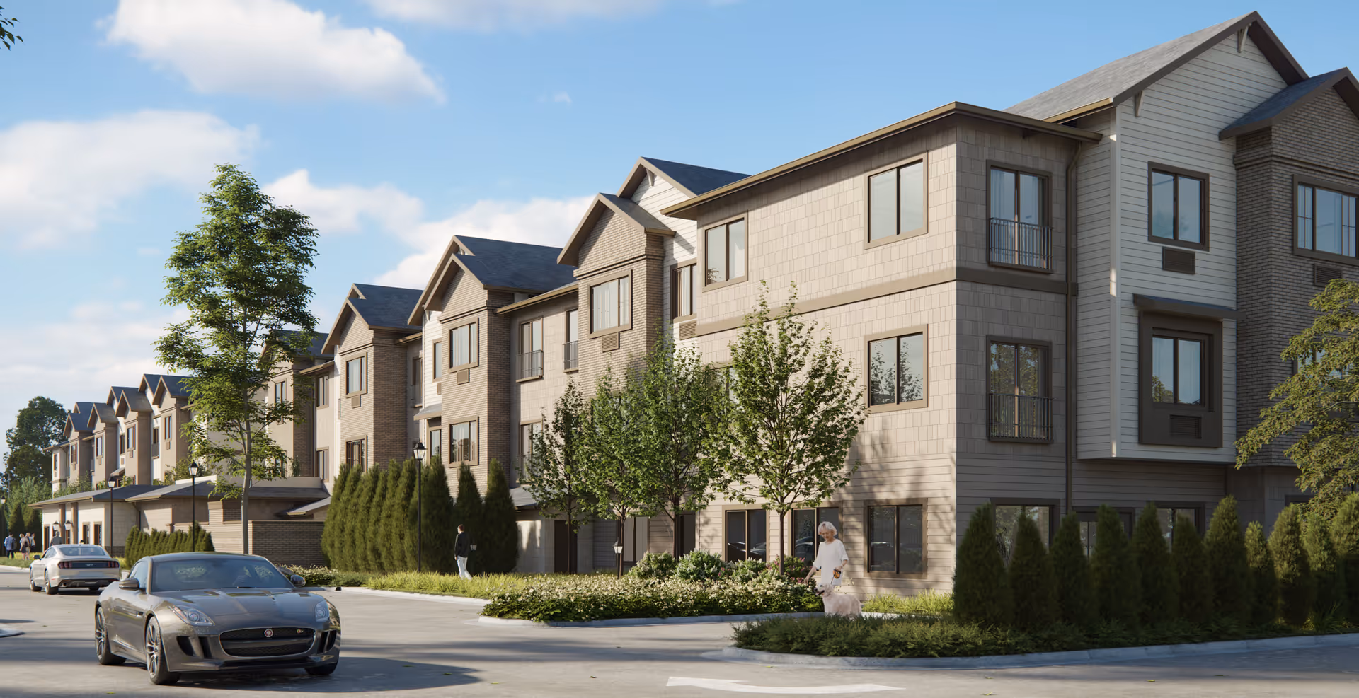 Exterior view of a multi-story senior living facility building with beige and brown siding, several windows, and small trees and shrubs along the sidewalk. A few cars are parked on the street, and a person is walking a dog near the entrance.