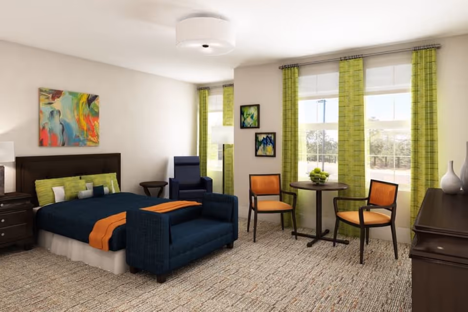 A well-lit bedroom featuring a bed with dark blue bedding and orange accents, a dark wood headboard, and green pillows. There is a dark blue armchair and a small round table with two orange cushioned chairs near two large windows with green curtains. The room also includes a dark wood dresser with decorative vases, colorful abstract paintings on the walls, and a beige carpeted floor.