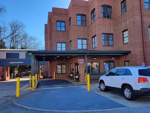 Brick multi-story senior living building entrance with a covered drop-off canopy and a parked white SUV.