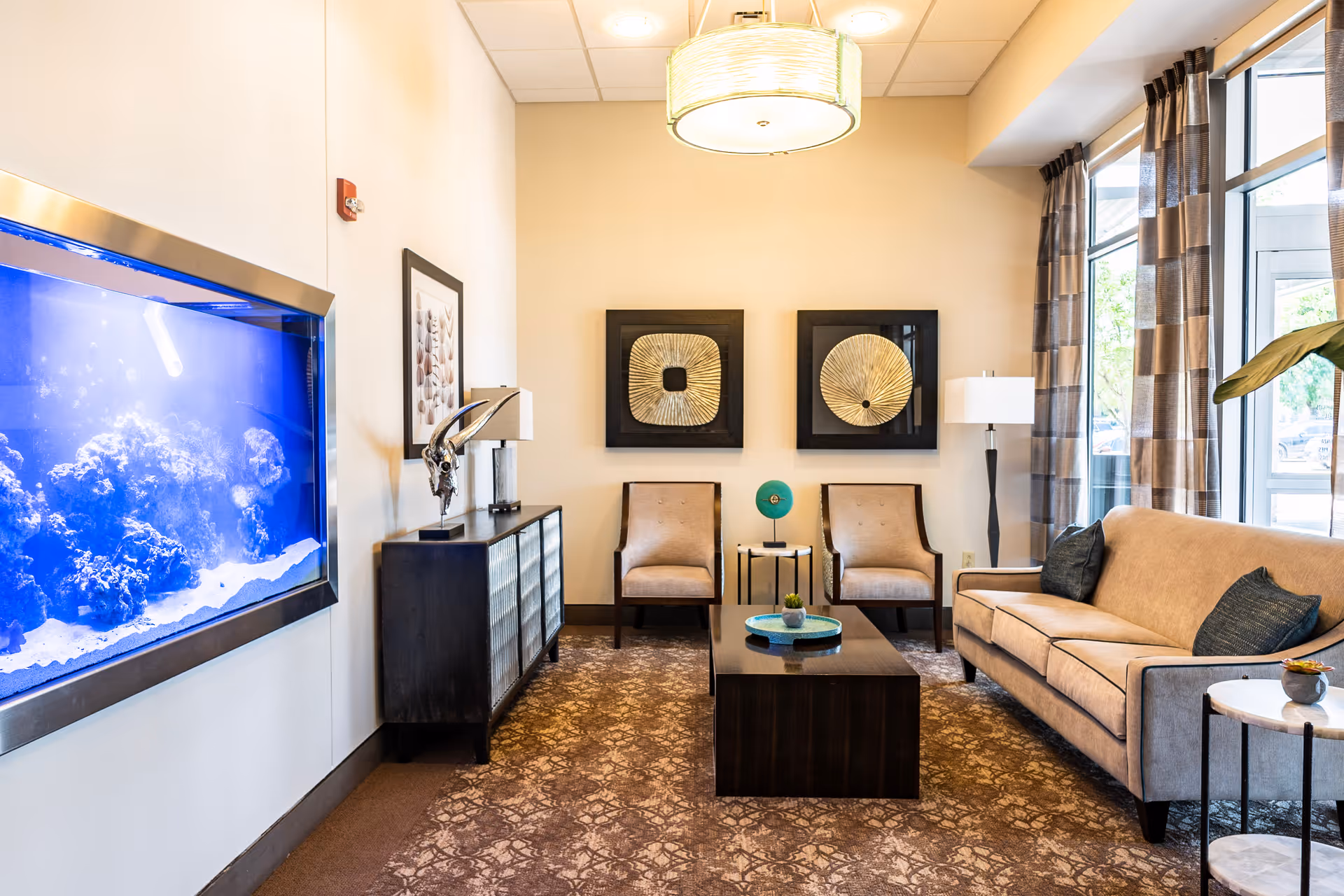 A bright sitting room with a sofa, two chairs, coffee table, wall art and a large built-in aquarium.