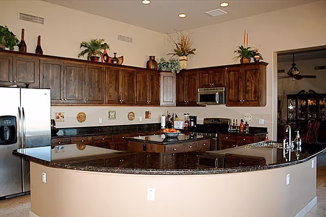 Spacious kitchen with a curved granite countertop, wooden upper and lower cabinets, a central island, and stainless steel appliances.