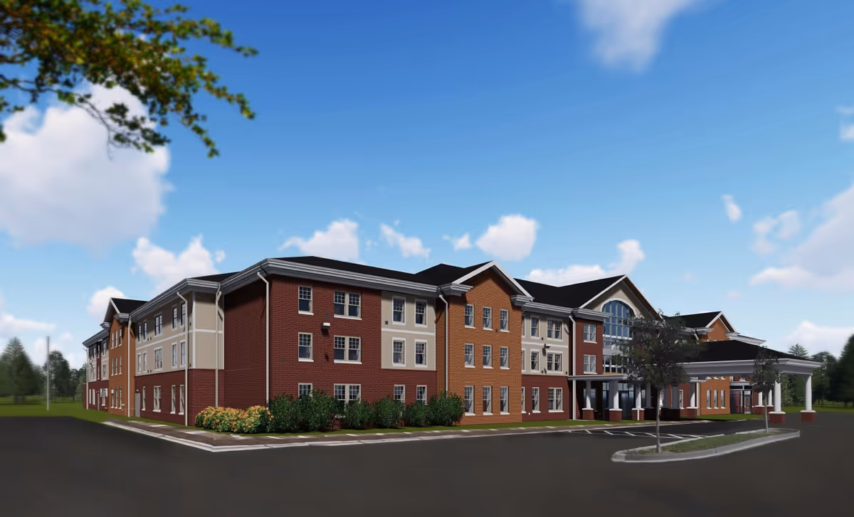 Exterior view of a large three-story senior living facility building with a brick and beige facade, multiple windows, a covered entrance, and surrounding greenery under a blue sky with scattered clouds.