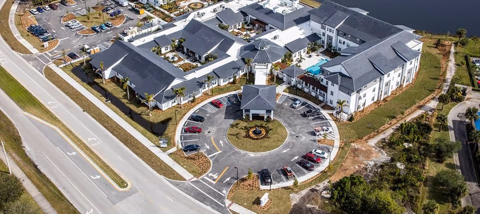 Aerial view of a senior living facility with a circular drive, parking lot, multiple connected buildings and surrounding roads and landscaping.