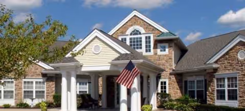 Front exterior of a brick senior living facility with columns and an American flag.