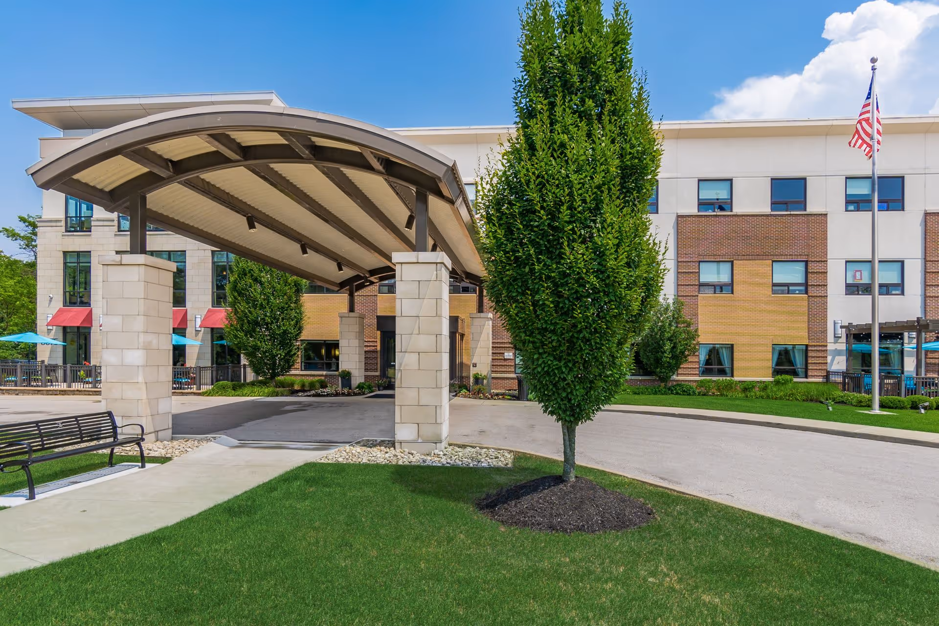 Modern senior living facility exterior with curved entrance canopy and green landscaping.