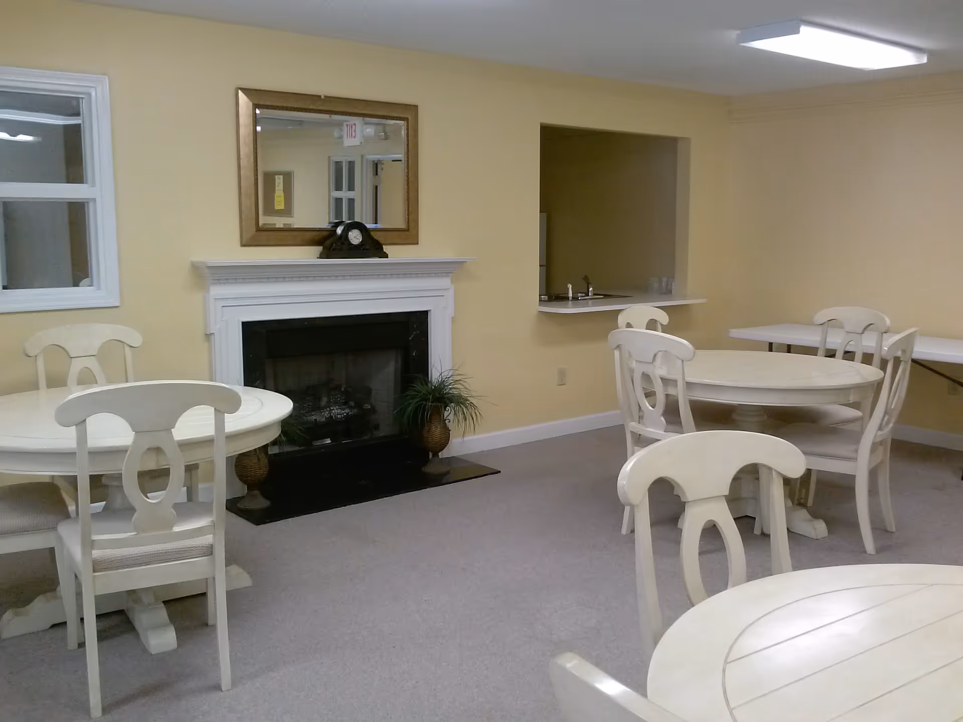 Small common room with round dining tables and chairs, a fireplace, and a pass-through counter to a kitchenette.