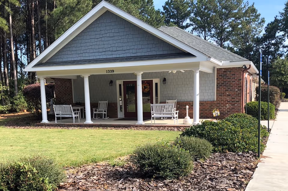 Front exterior of a single-story brick and siding building with a covered porch, white columns, benches, and the address number 1339.