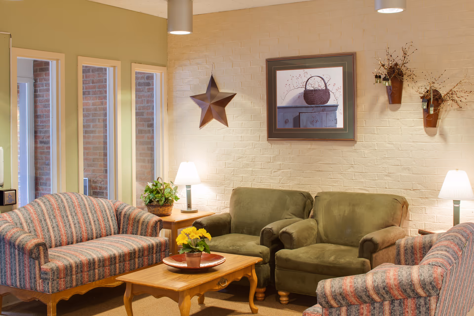 Cozy living room with patterned sofas, two green armchairs, a wooden coffee table with a potted plant, table lamps, and wall decor.