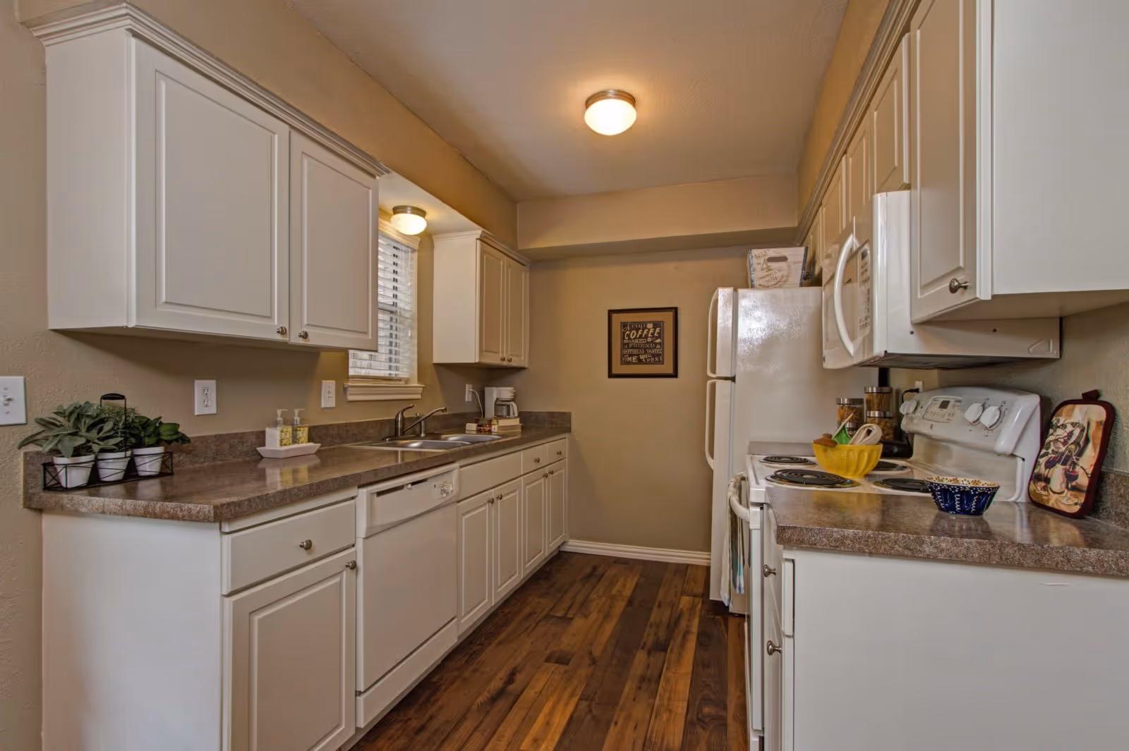Galley-style kitchen with white cabinets, laminate countertops, a stove, refrigerator, sink and wood-look flooring.