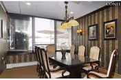 Formal dining room with a long dark table, upholstered chairs, chandelier, patterned wallpaper and large window with blinds looking out to a patio.