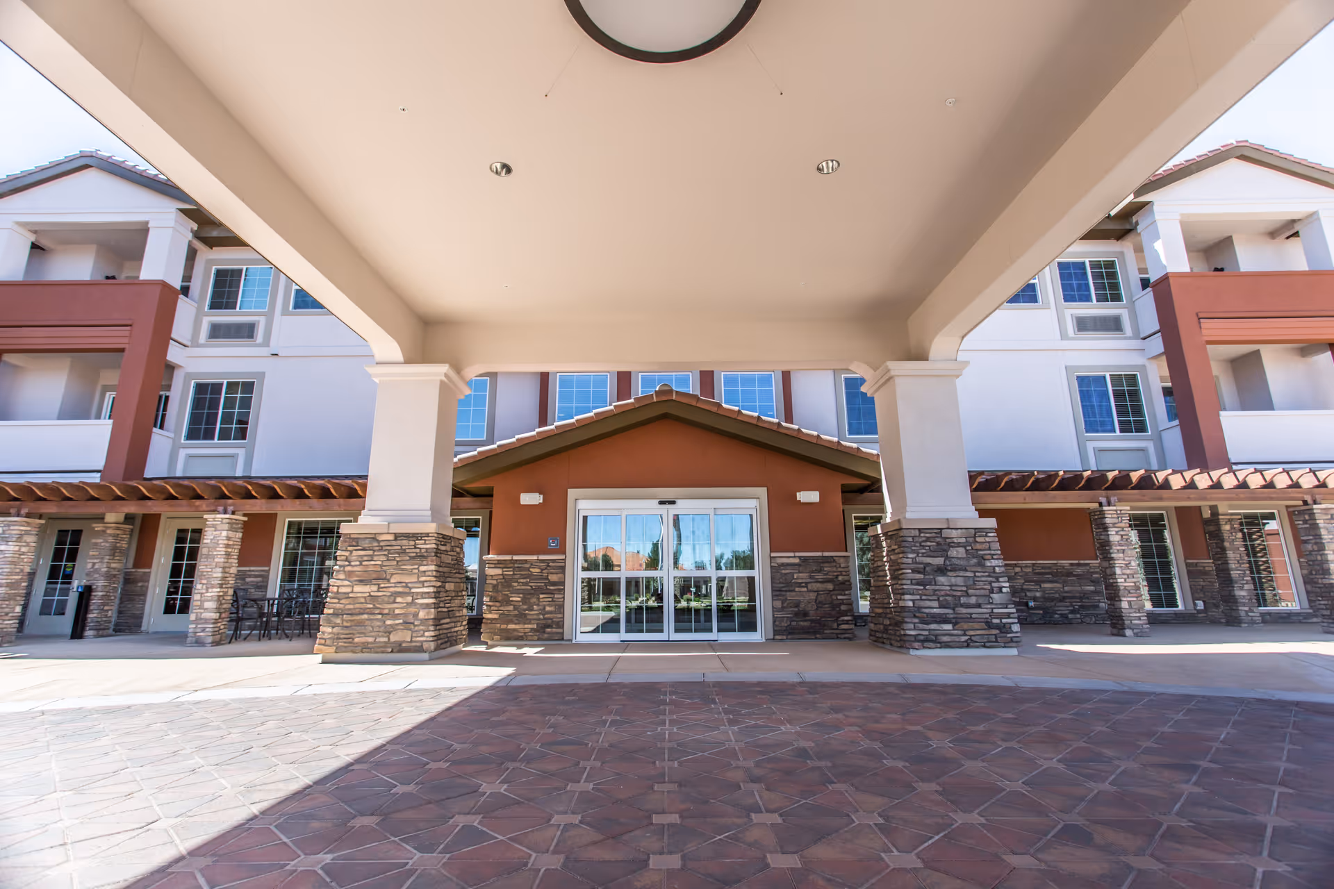 Covered entrance and front facade of a multi-story senior living building with stone columns and sliding glass doors.