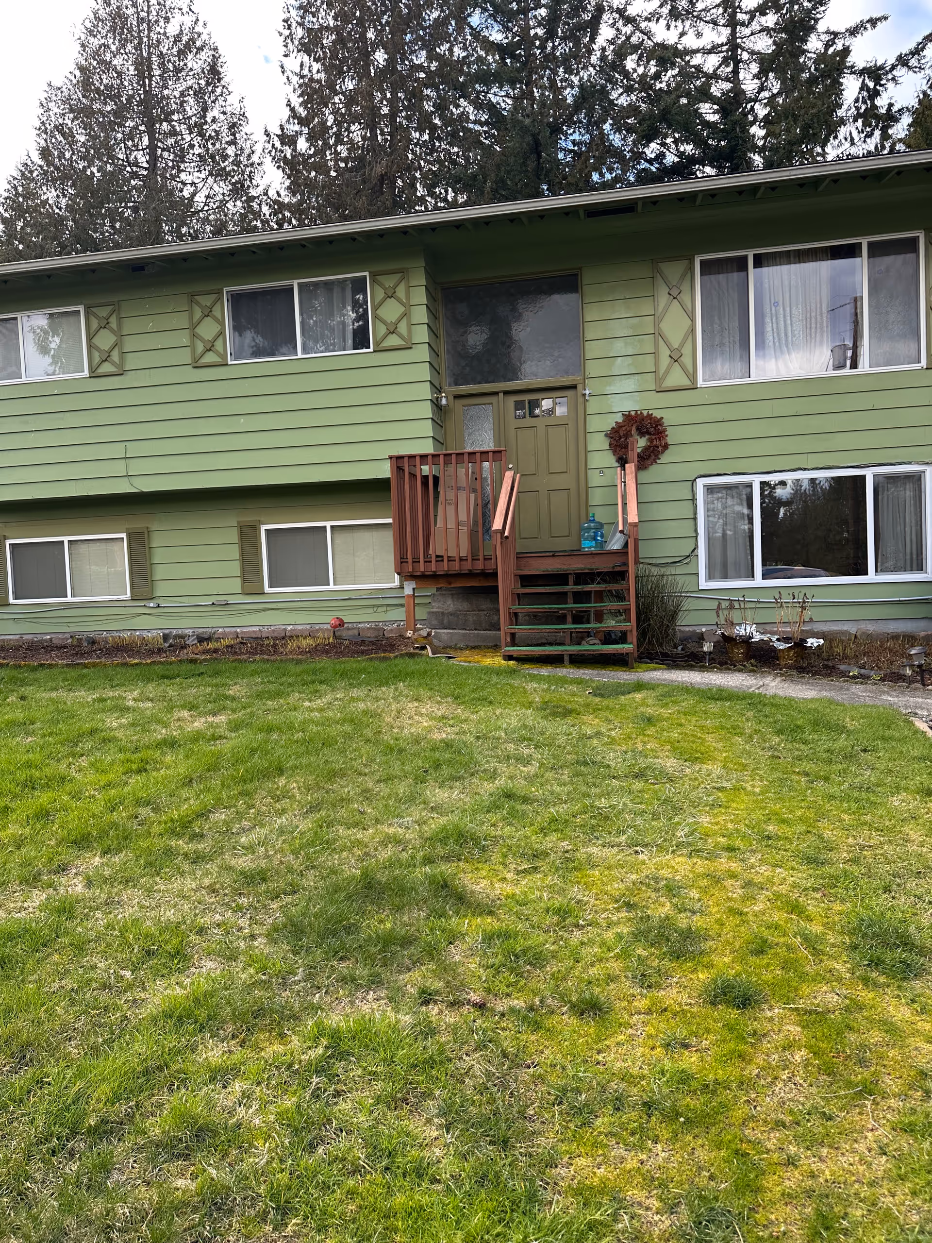 Front exterior of a green two-story house with a small wooden porch and a grassy front lawn.
