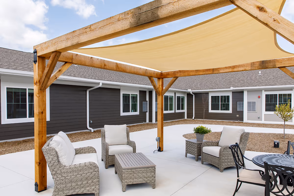 Outdoor courtyard with a wooden pergola and shaded seating area in front of a single-story building.