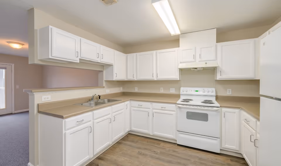 Bright U-shaped kitchen with white cabinets, beige countertops, and an electric stove.