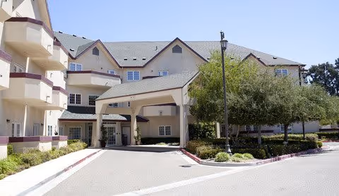 Front entrance of a multi-story senior living building with a covered drop-off driveway and surrounding landscaping.