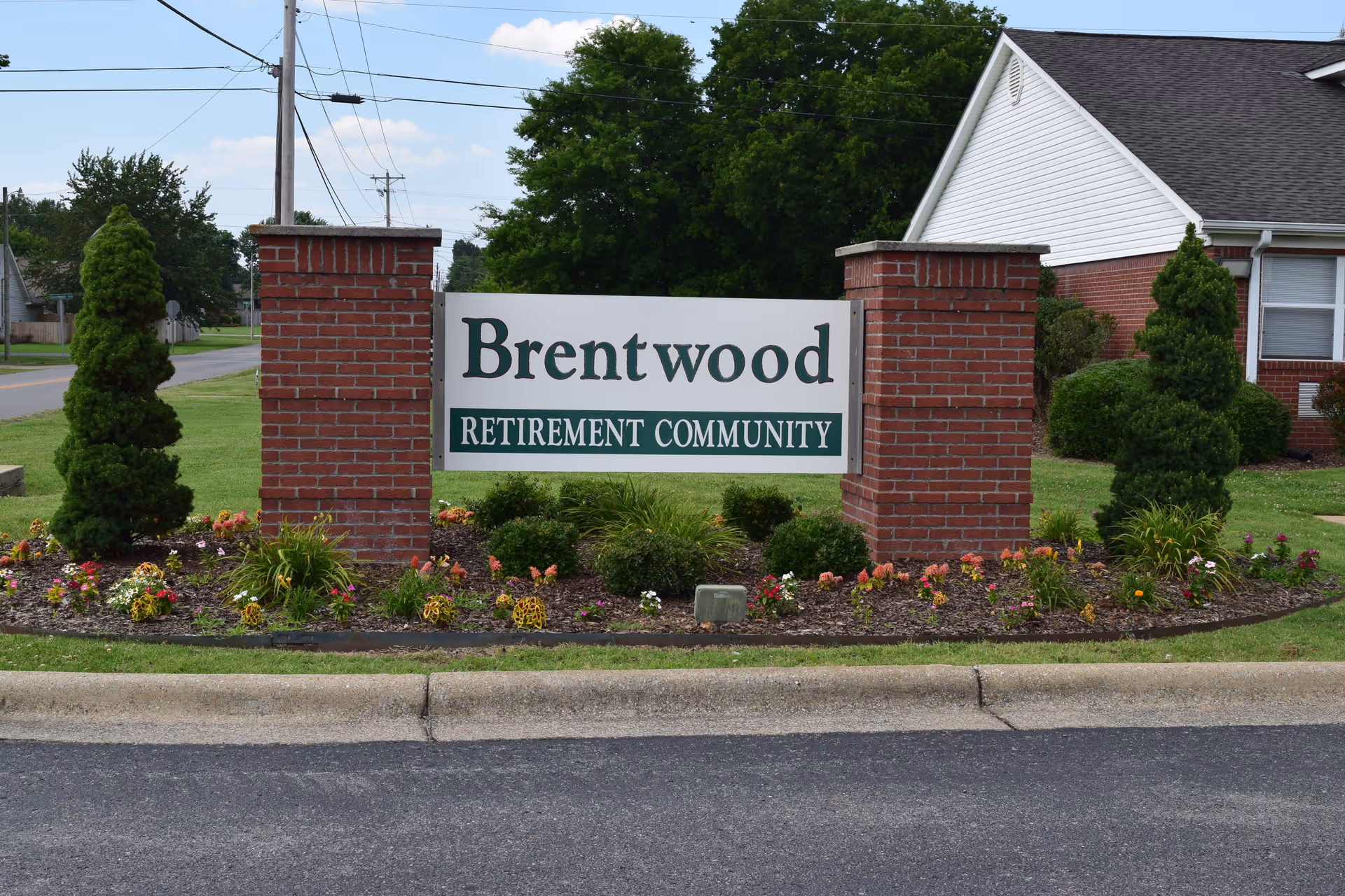 Brick-pillared entrance sign reading 'Brentwood Retirement Community' surrounded by landscaping and a nearby residential building.