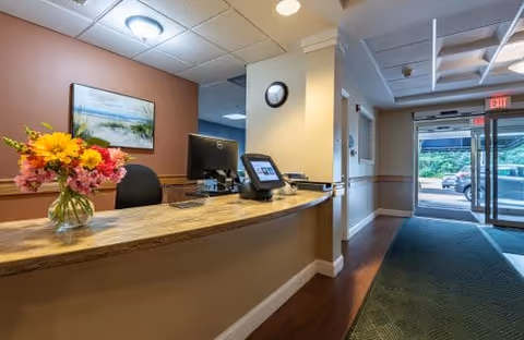 Reception desk and lobby area with a floral arrangement, computer monitors, and glass entry doors leading outside.