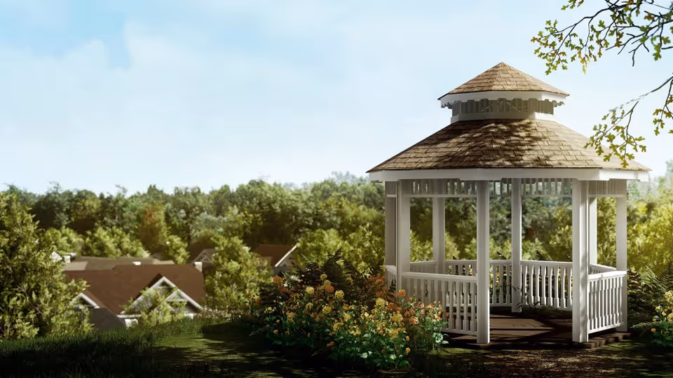 White wooden gazebo on a grassy hill surrounded by flowers and trees with rooftops visible in the background.