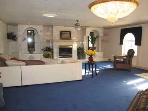 Spacious senior living room with blue carpet, fireplace, chandelier, and comfortable seating.