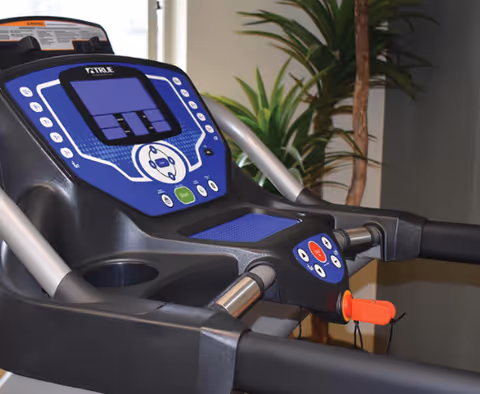 Close-up view of a treadmill control panel with buttons and a digital display, situated indoors near a potted plant.