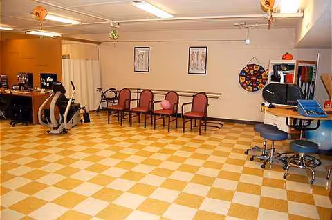 Bright Pleasant Manor senior living multipurpose room with row of chairs, exercise equipment, and activity area.