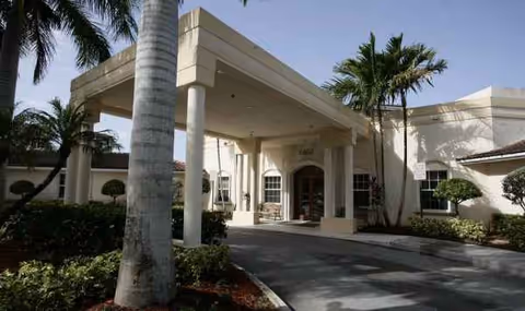 Entrance of HarborChase of Tamarac with a porte-cochère and palm trees.