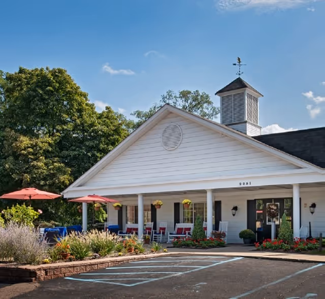 White senior living facility with a covered front porch, colorful chairs, and flowers.
