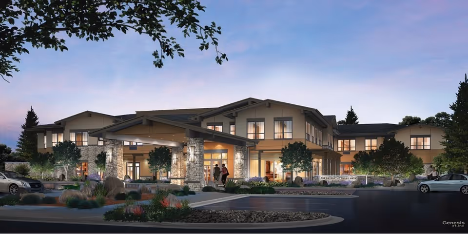 Exterior view of a two-story senior living facility named Retreat at Sunny Vista during dusk, featuring a covered entrance with stone pillars, landscaped greenery, and parked cars in the foreground.