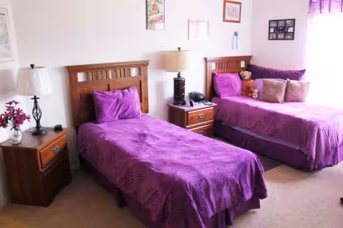 Two twin beds with purple bedding and matching nightstands in a bright bedroom.