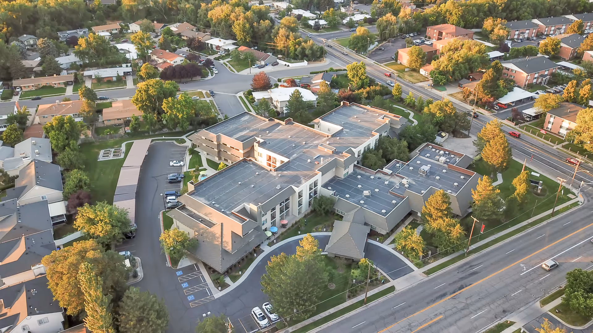 Aerial view of Cottonwood Creek senior living facility surrounded by trees and residential houses, showing multiple connected buildings with parking lots and roads nearby.