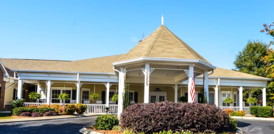 Sunlit, single-story senior living building with a large front porch and manicured shrubbery.