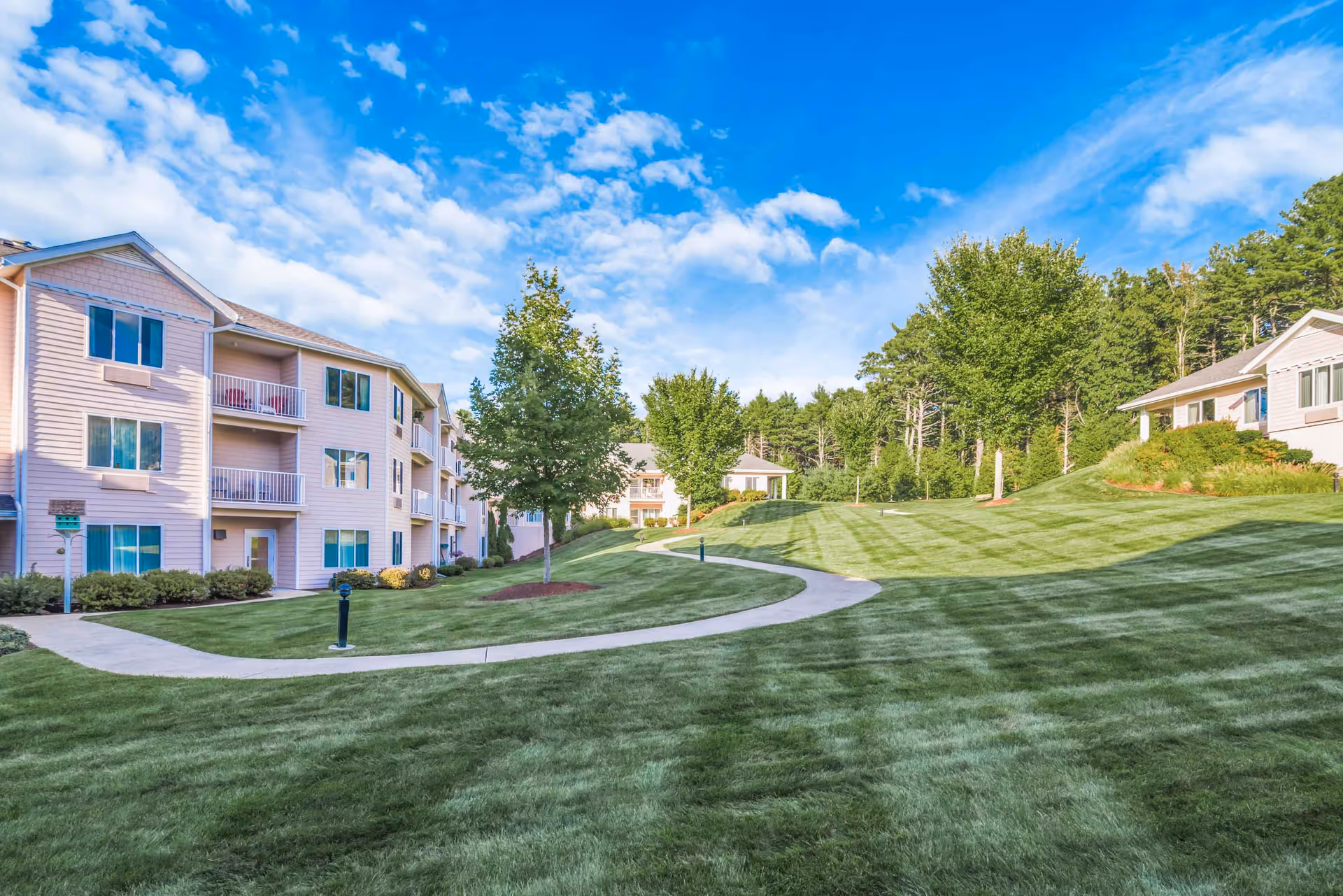 Well-maintained grassy courtyard with a curved walkway and multi-story residential buildings under a blue sky.