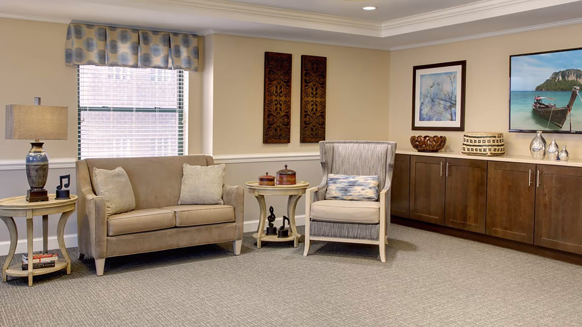 Cozy sitting area with a loveseat, upholstered armchair, side tables and built-in cabinets in a communal living room.