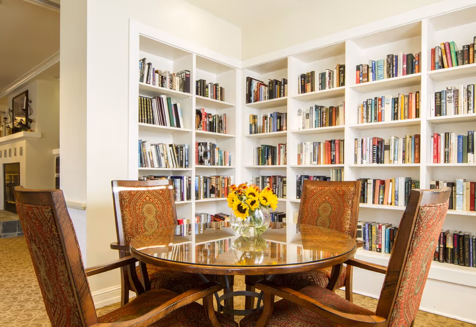 Round wooden table with four upholstered chairs and a vase of sunflowers in front of built-in white bookshelves.