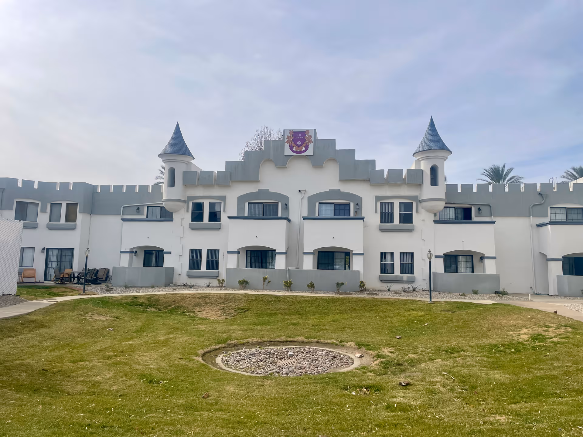 Front exterior of a white, castle-styled senior living building with turrets and a grassy courtyard.