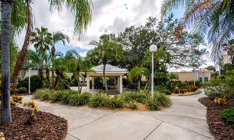 Landscaped courtyard with palm trees, a central covered gazebo, paved walkways and lamp posts.