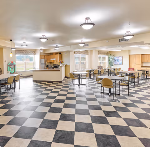 Spacious communal dining area with a black-and-white checkered floor, multiple tables and chairs, and a kitchenette at the back.