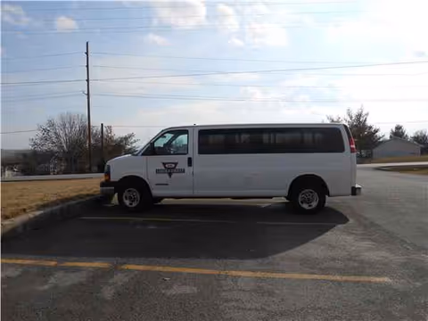 White passenger van parked in a paved lot beside a curb under a blue sky.