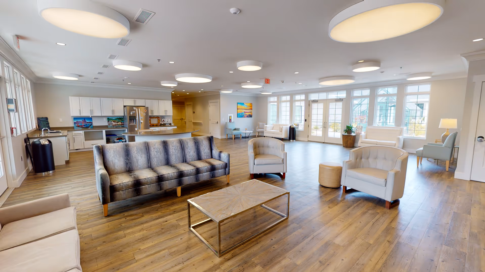 Spacious bright communal living area with sofas, armchairs, a coffee table, and a kitchenette in the background.