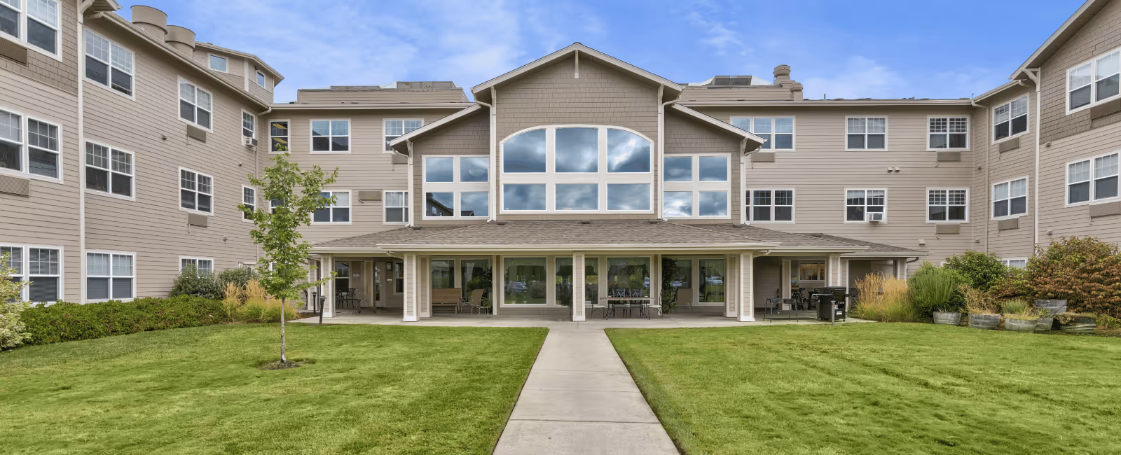 Front exterior view of Cascades of Grants Pass, a multi-story beige senior living building with a central entrance and a grassy courtyard.