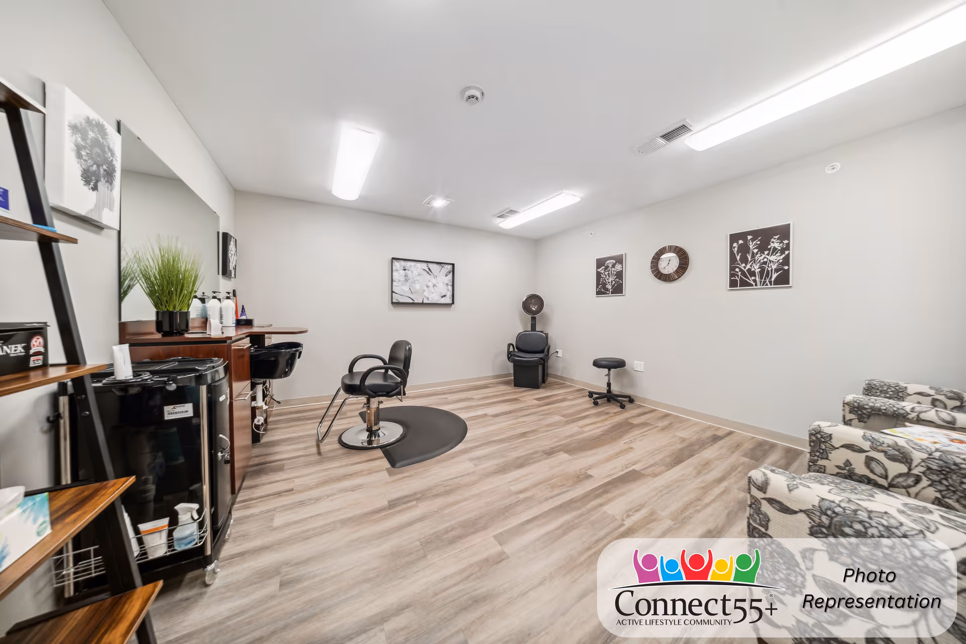 Bright salon-style room with styling chairs, a shampoo sink, shelving and upholstered waiting chairs in a senior living community.