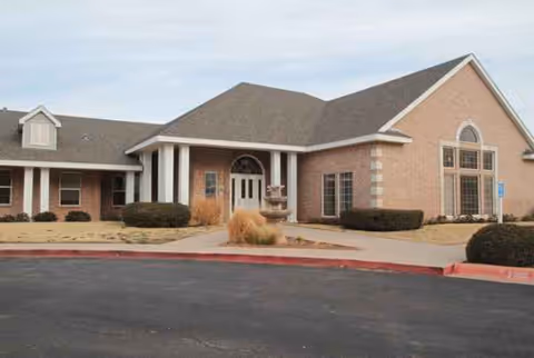 Exterior view of a brick senior living facility entrance with columns, windows, and landscaped surroundings.