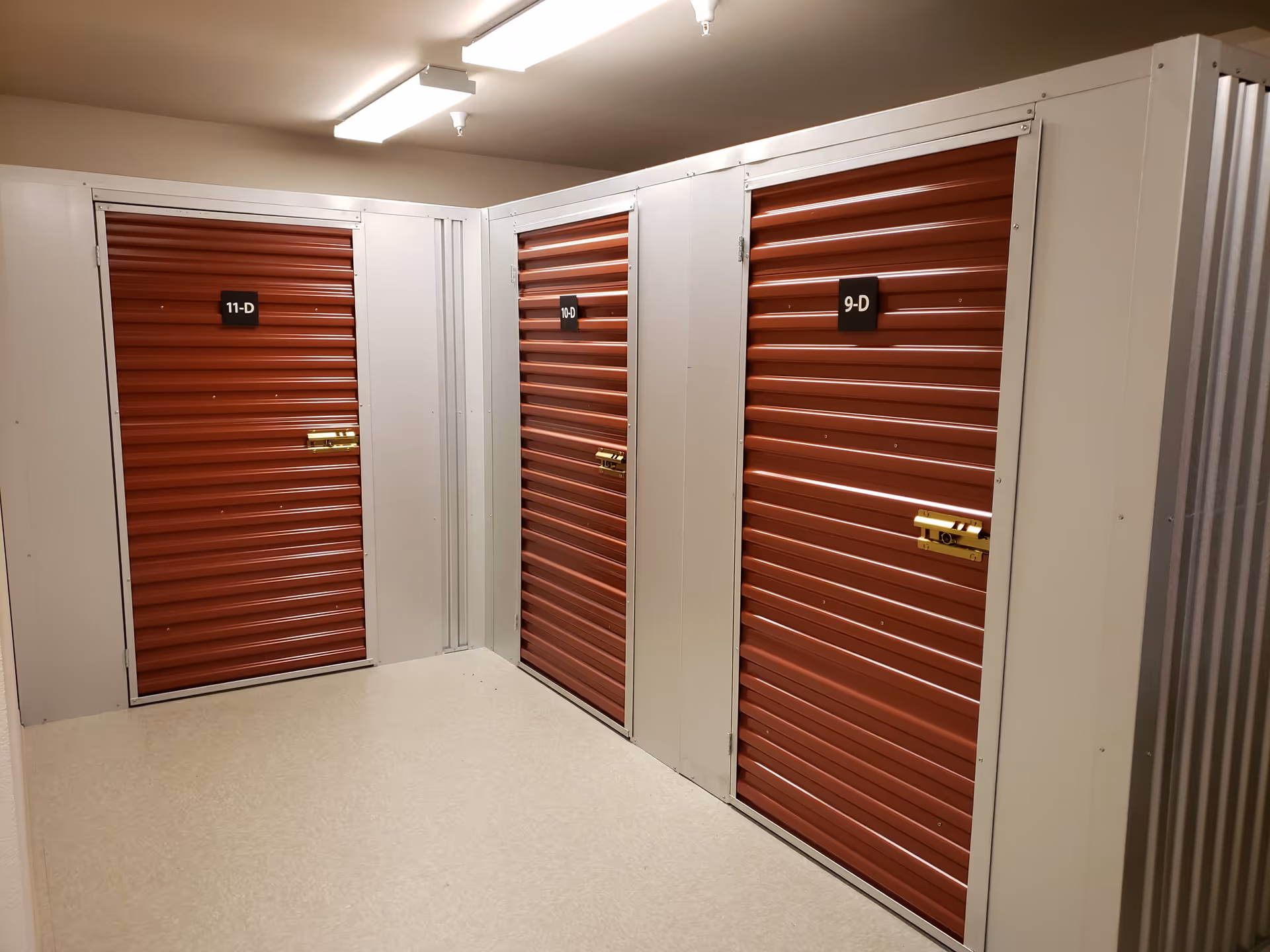 Indoor hallway with three red roll-up storage unit doors labeled 11-D, 10-D, and 9-D.