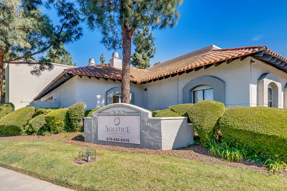 Exterior front of a low-rise stucco building with a tiled roof, manicured shrubs, and a sign reading "Solstice Senior Living".