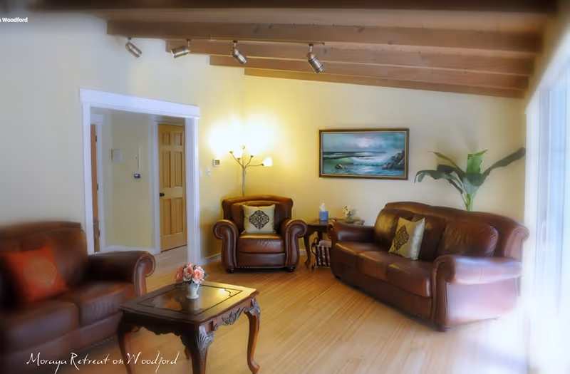 Cozy living room with leather sofa and armchairs, a wooden coffee table, wall art, and exposed beam ceiling.