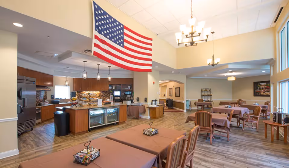 Spacious dining area with multiple tables and chairs, a serving counter and open kitchen, and an American flag hanging from the ceiling.