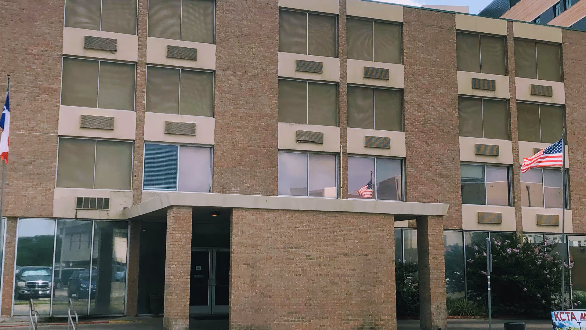 Brick multi-story building front with a covered entrance, rows of windows, and American flags.