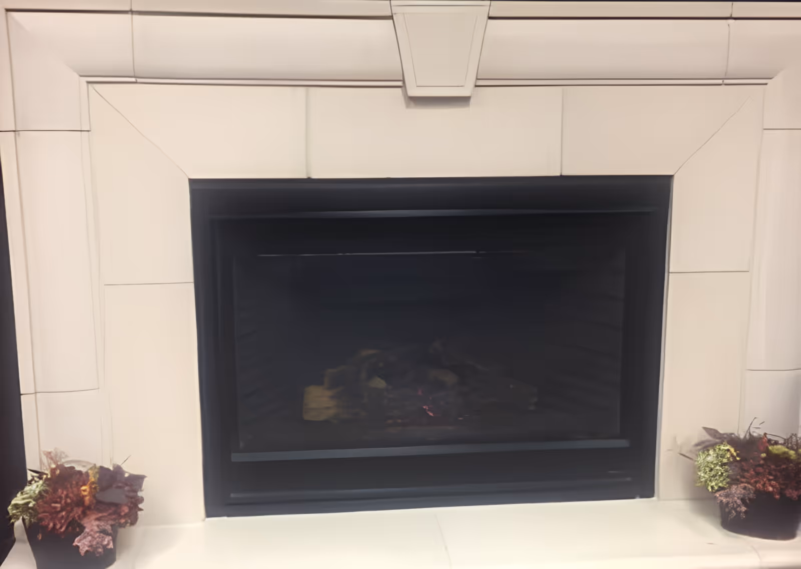 A modern tiled fireplace with a black firebox and potted plants on each side.